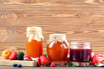Fototapeta na wymiar Sweet jam in glass jars with ripe berries on brown wooden table