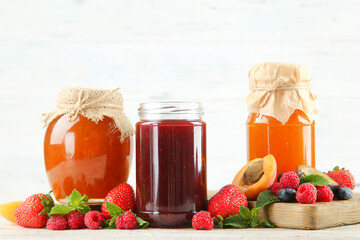 Sweet jam in glass jars with ripe berries on white background