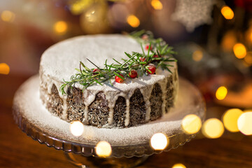 Christmas homemade cake with rosemary and cranberries stands on a wooden table against the of a decorated Christmas tree