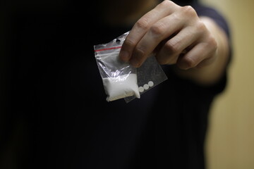 A white-skinned girl, as she holds out two clear plastic bags in front of her, containing powdered cocaine and illegal smuggled drugs.