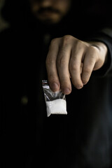 A Caucasian boy, holding his arm outstretched forward, while holding a transparent sachet with...