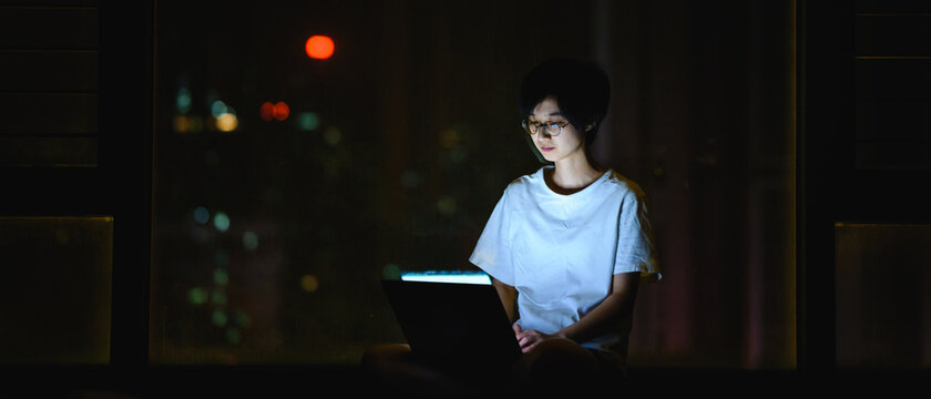 Girl using laptop at night by the window