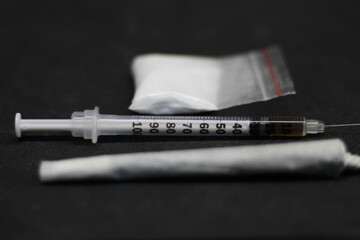 A syringe full of cocaine, placed in the center between a marijuana joint and a sachet full of...