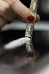 A close-up front image of a woman cocaine addict, holding a rolled dollar bill with her fingertips,...