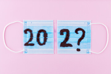 Text 202 on pink background and surgical mask. Concept of the New Year with blue protective mask. Celebrating New Year in quarantine, covid-19. Top view. Copy space