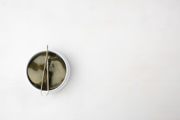 Top view on the jar with gold collagen hydrogel eye patches and tweezers on the white background with copy space.