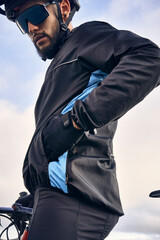 Young cyclist in sport clothing, glasses and helmet sitting on his bike with his hand in the pocket of the windbreaker jacket. Concept of activities and motivation.