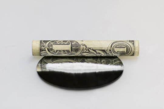Close-up front close-up photo of a rolled up dollar bill, for snorting the cocaine powder strip placed on a round mirror