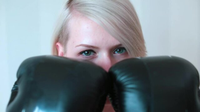 A woman in boxing gloves poses for the camera. He covers his face with gloves. Warm up before hand training. Healthy lifestyle.
