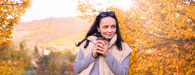 A beautiful woman with a coffee to go walks in the autumn park. Walking outdoors on a nice day. Banner, long format. High quality photo. Copy space - Powered by Adobe