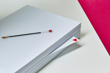 A ream of white A4 paper sits on a desk with a love heart scribbled on a single page.