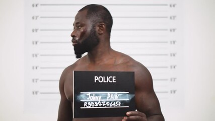 In a police station african arrested beaten man poses for front view mugshot.