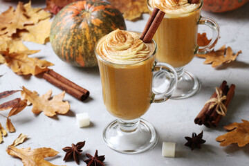 Two glass cups pumpkin latte with spices and creamy foam on grey background with pumpkins and...