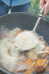 Cooking pilaf in a cauldron on the grill outside in the summer