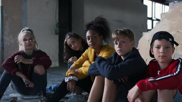 Group of teenagers gang sitting indoors in abandoned building, looking at camera.