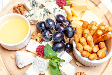 Fototapeta na wymiar Board with different types of cheese. Cheeses mix set dor blu chedar parmesan brie honey sauce finger bread and grape on wooren palte. Restaurant menu breakfast plate. Healthy snack assortment.