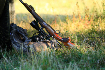 Hunting professional equipment. Hunter binoculars, rifle and Bag laid on the grass in the forest.