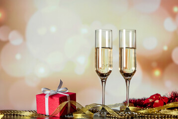 New Year's eve celebration. Two glasses with champagne with a gift and decorations against holiday lights. Toasting. Christmas background. Christmas card, greeting. Copy space. Blurred lights. Bokeh