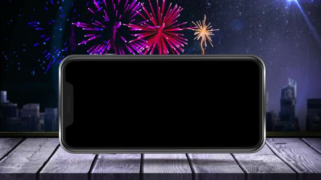 Digital animation of smartphone on wooden surface against fireworks exploding over cityscape