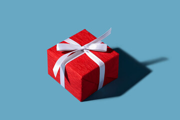 Red gift box with white ribbon and bow on the blue background. Christmas and New Year concept. Greeting and celebration. Isolated. Isometric.