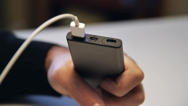 Close up of hand inserting a USB cable charger into portable power bank. Media. Close up of mans hand inserting a cable into charger.