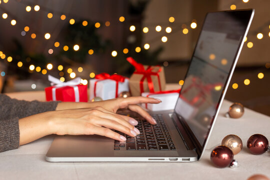 Christmas shopping online, sales and discounts promotions during winter holidays, online shopping at home and lockdown coronavirus. Female hands on the laptop with gifts and blurred bokeh lights