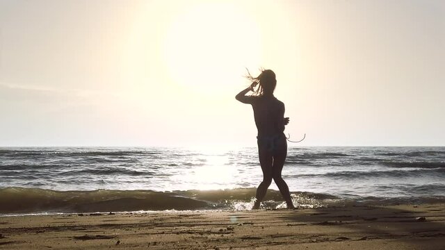 silhouette girl in a bikini on a beach at sunset, having fun, jumping and dancing. slowmotion recorded at 120fps