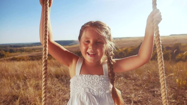 little girl kid swinging on a wooden swing on a tree in the park. happy family kid dream concept. little kid girl playing on fun wooden swing on tree dream concept in fun park