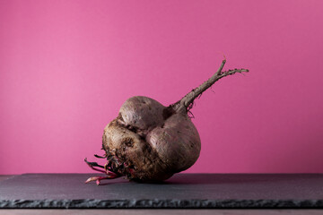Ugly beetroot on a pink background, close-up. Vegetables of unusual shape, reduction of food organic waste