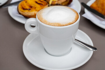 Cup of cappuccino coffee served with traditional dessert pastry in Portugal, nata eggs cream cakes with fruits