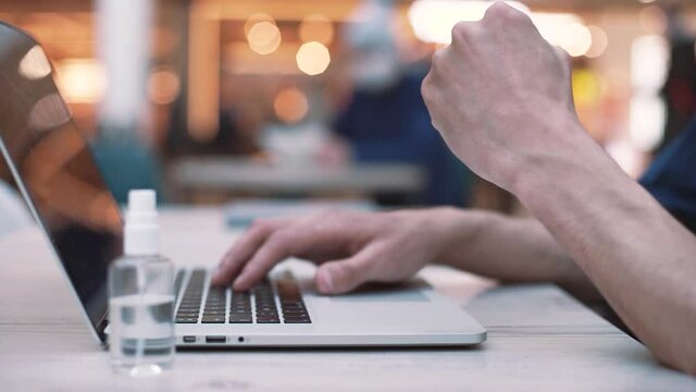 young man is working typing a message on a laptop while sitting in a cafe . close - up .