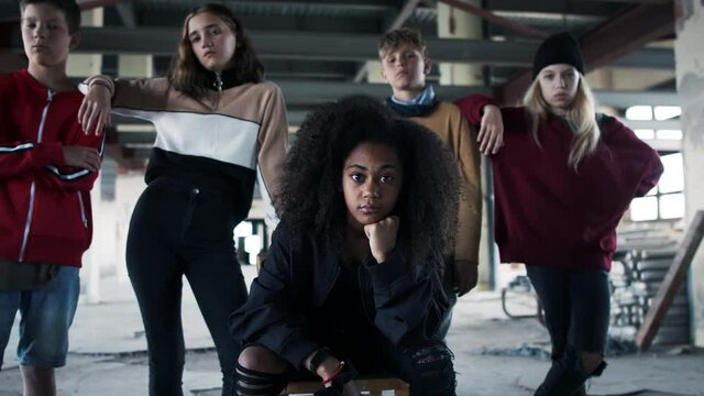 Group of teenagers gang standing indoors in abandoned building, looking at camera.