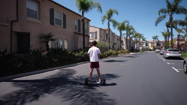 Video of a boy rides a hoverboard in a residenital neighborhood
