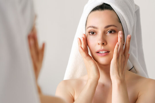 A natural woman with good skin holds her cheeks and looks in the mirror. SPA, cosmetology, beauty