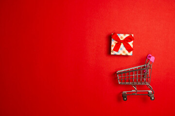 Supermarket cart and gift box with red ribbons on red background
