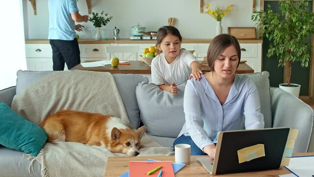 Social Distancing. A Busy Mother Tries to Work Remotely with Her Child and Husband at Home. The Daughter Interferes with Her Mother's Work. In the Background, Dad is Busy in the Kitchen.