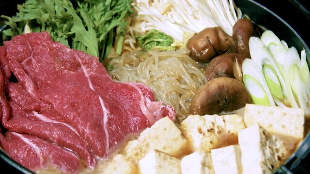 Japanese traditional winter hot nabe dish Sukiyaki with raw meat and v