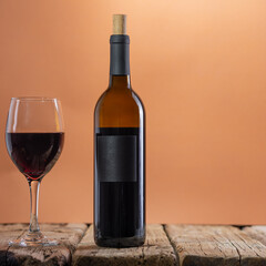 Bottle and glass with red wine on rustic wooden table on beige background. Concept of alcoholic drink. Photo for advertising and product promotion. Space for text.