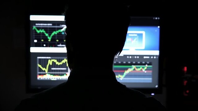 A silhoutte of a man in front of a screen looking at stock market index charts. HD 24FPS.