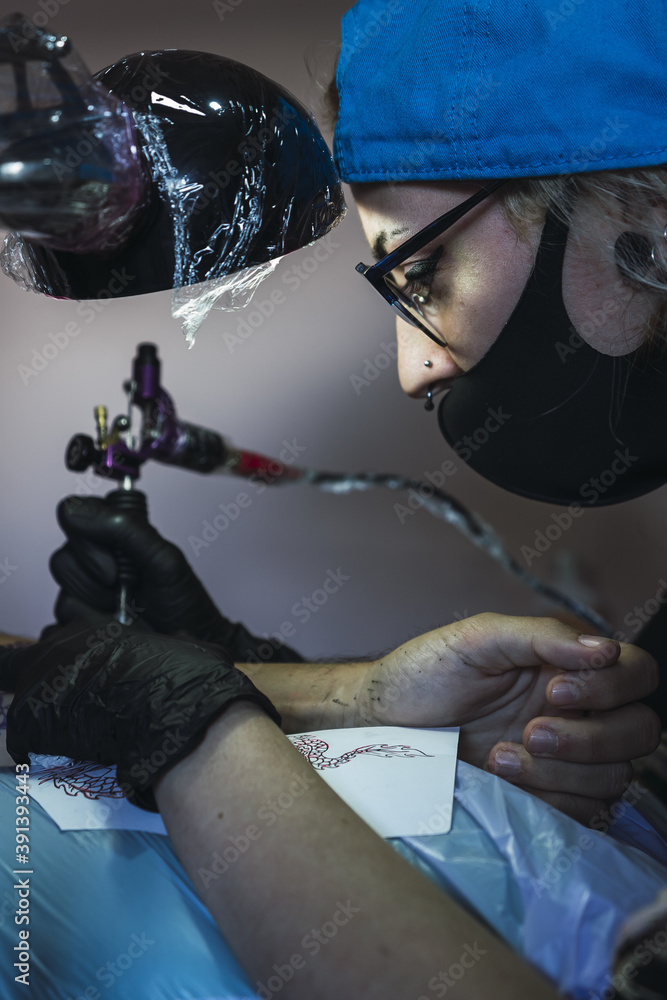 Wall mural Female tattoo artist tattooing a dragon on a man's arm