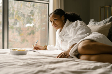 Black woman journaling at home in bed