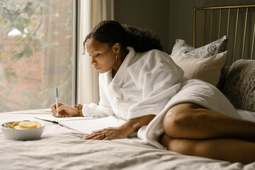 Black woman journaling at home in bed