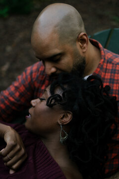 Black mand and woman in love outdoors in backyard sitting next to cozy firepit