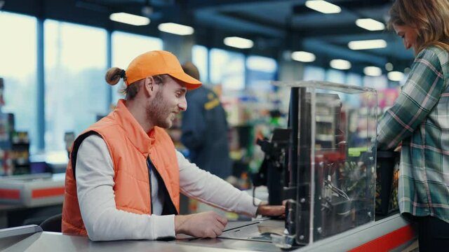Young caucasian man cashier person working at supermarket communicating with customer. Beautiful woman putting goods on line enjoying friendly services.