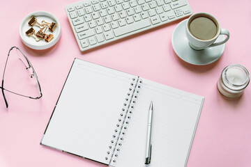 Cozy woman workplace with blank notepad, keyboard, cup of coffee, glasses and candle. Top view, flat lay