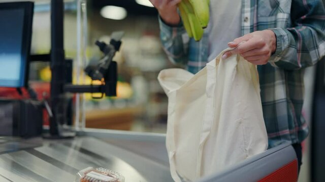 Medium shot of woman sorting and packing her food items in eco friendly bag at cash register. Supermarket food shopping. Eco shopping. Modern lifestyle.
