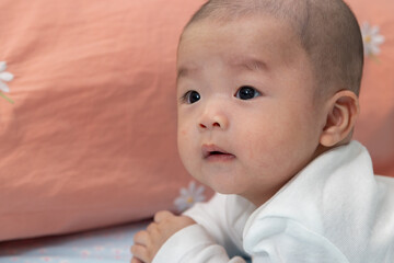 Adorable and happy Chinese baby boy on tummy time on bed. Newborn child relaxing in bed