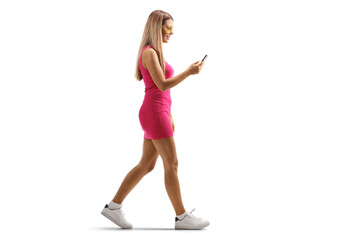 Full length profile shot of a young woman in a mini pink dress walking and using a smartphone