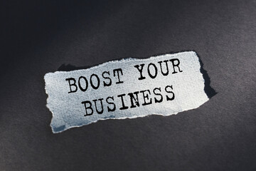 BOOST YOUR BUSINESS - text on torn paper on dark desk in sunlight.