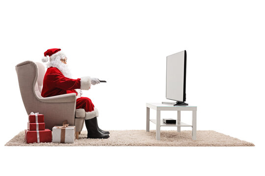 Full length profile shot of santa claus in armchair with a remote control watching tv